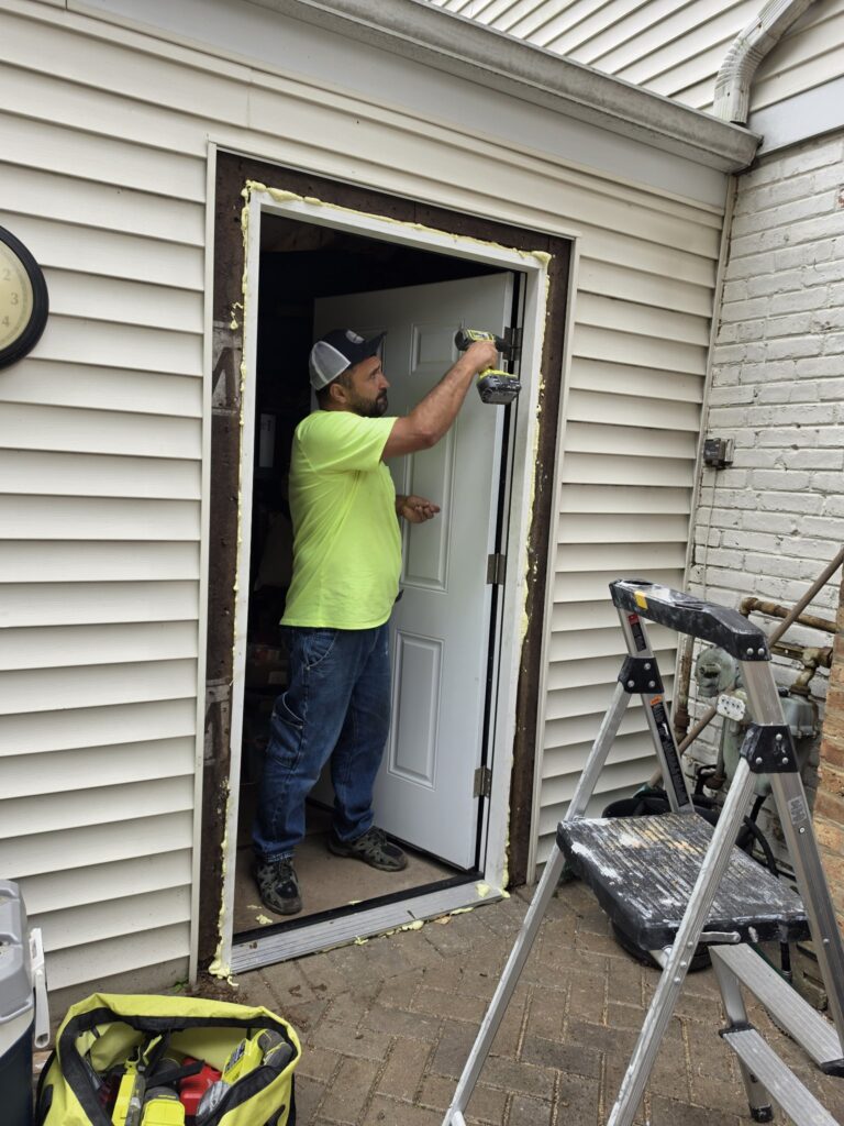 Door installation Chicago — drilling hinges into a foam-sealed door frame